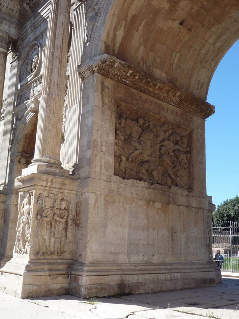 Le côté Ouest de l'intérieur de l'arcade centrale avec l'inscription "LIBERATORI · VRBIS" (libérateur de la cité) au dessus d'un fragment de frise représentant la conquête d'un village dace par la cavalerie et l'infanterie romaine qui poussent les prisonniers.