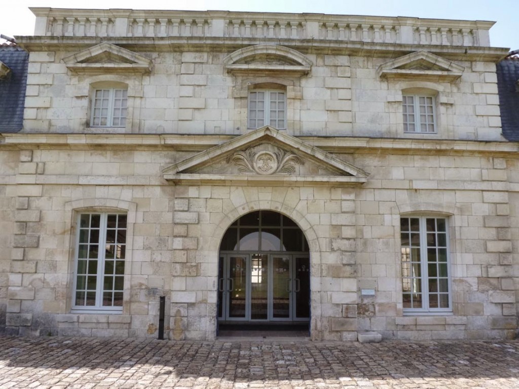 La façade du petit bâtiment est interrompu en son centre par la seule élévation à deux niveaux (Le fronton est décoré du monogramme de Louis XIV).