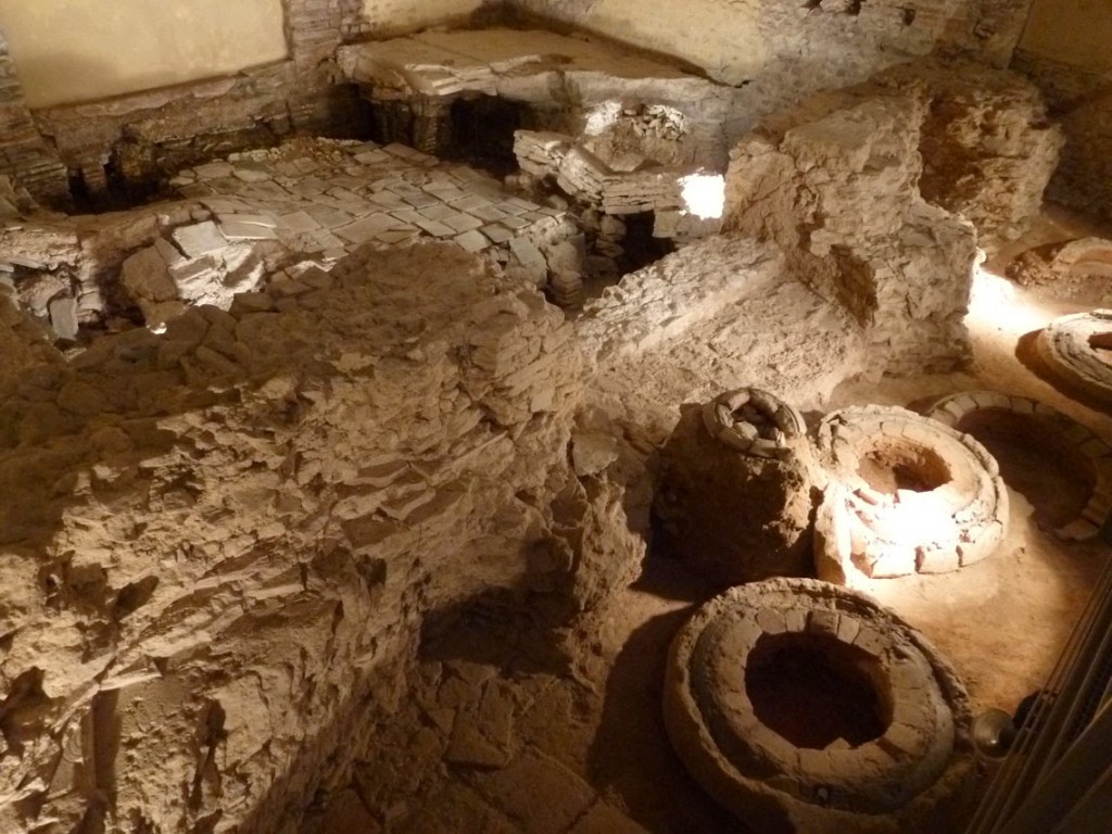 Des vestiges de la construction de l'église sont également présents comme ces anciens moules à cloche. Derrière se trouve les restes du mur nord des thermes, et le caldarium dont la suspensura (sol au dessus de l'hypocauste) s'est effondré. Le côté Ouest de cette pièce chaude (en haut de la photo), était occupée par un bassin.